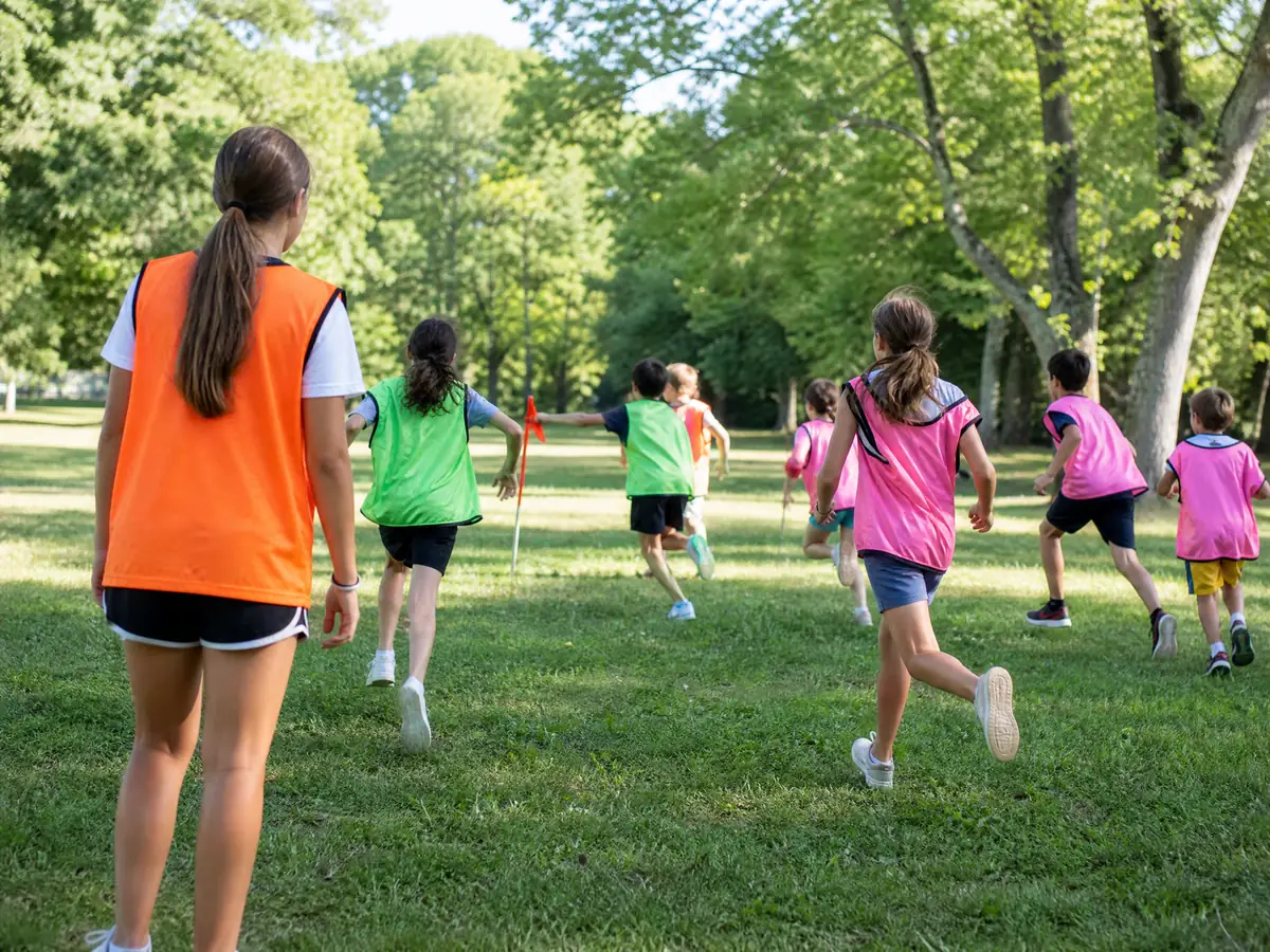 Enfants d'un centre de loisirs vus de dos jouant dans un parc, en chasubles vertes et roses